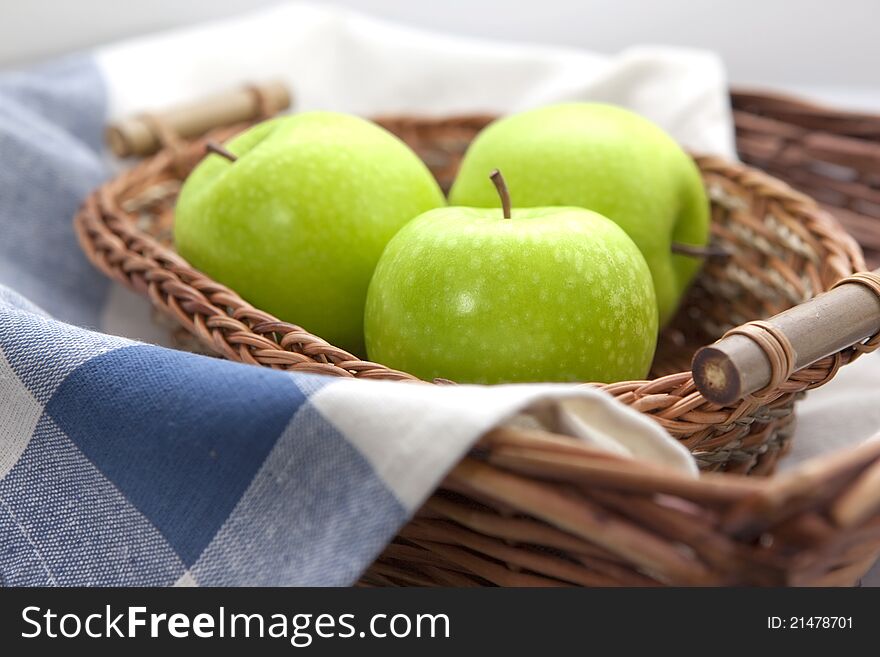 Green apples in the brown wicker basket with a blue gingham cloth