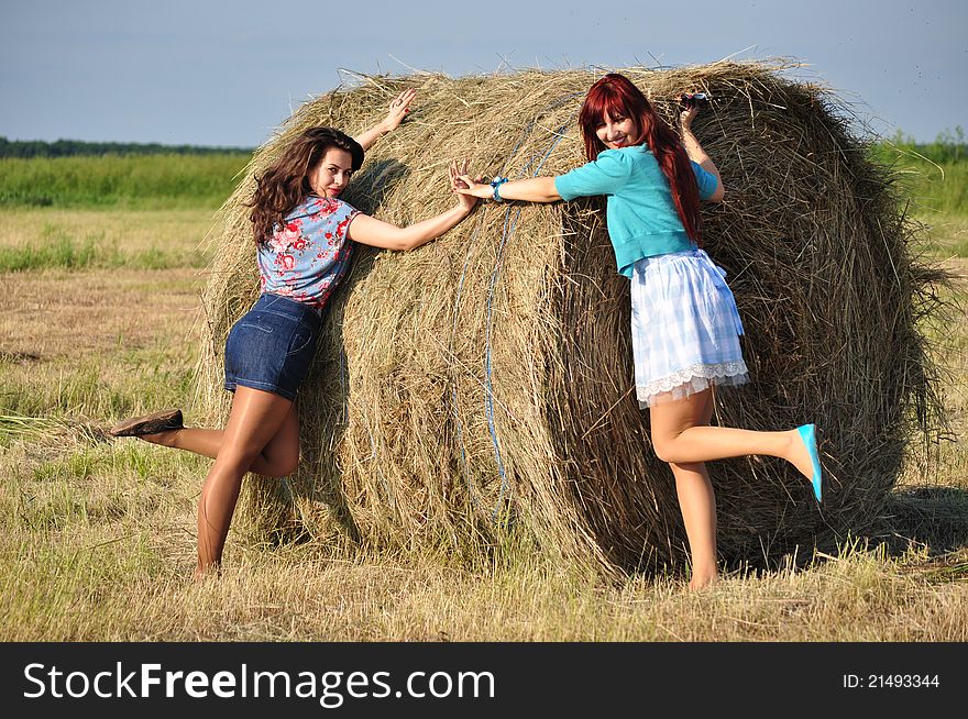 Two young girls standing by haystacks.