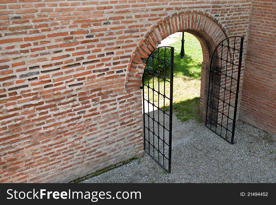 Opened iron forged gate with brick wall