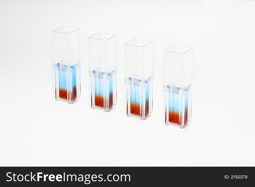 Four quartz cuvettes in perspective that contain two liquid phases for a biotechnological colour comparative analysis on a white background. Biological samples can be observed in the blue and red/brown liquids. Four quartz cuvettes in perspective that contain two liquid phases for a biotechnological colour comparative analysis on a white background. Biological samples can be observed in the blue and red/brown liquids.