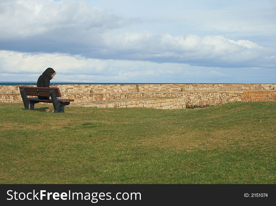 Lone person on a bench staring out to sea. Lone person on a bench staring out to sea.
