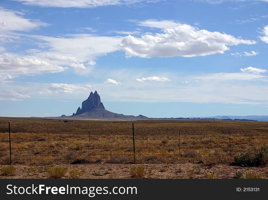 Shiprock monument from far away in New Mexico on a clear day with blue cloudy skies and other rocks in the background. Shiprock monument from far away in New Mexico on a clear day with blue cloudy skies and other rocks in the background