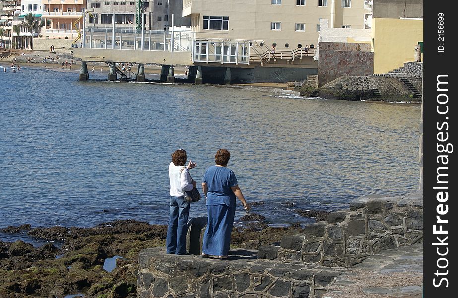 Two women looking at the scenery and rocky coast along the Atlantic Ocean with hotels and beaches across the harbour. Two women looking at the scenery and rocky coast along the Atlantic Ocean with hotels and beaches across the harbour