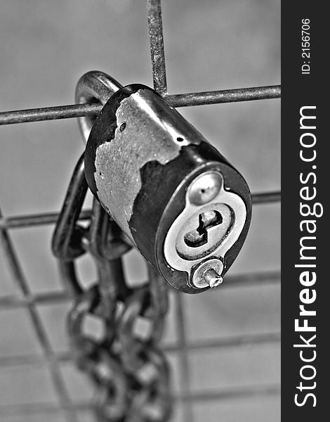 A black and white close up of a metal lock and chain on a fence. A black and white close up of a metal lock and chain on a fence