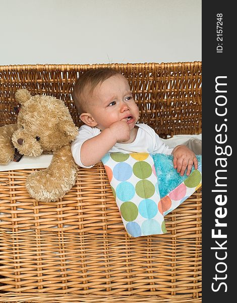 Image of cute baby and teddy bear peeking out of a wicker trunk