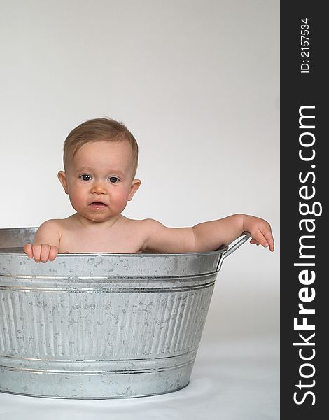 Image of cute baby sitting in a galvanized tub in front of a white background, holding his hands to his face. Image of cute baby sitting in a galvanized tub in front of a white background, holding his hands to his face