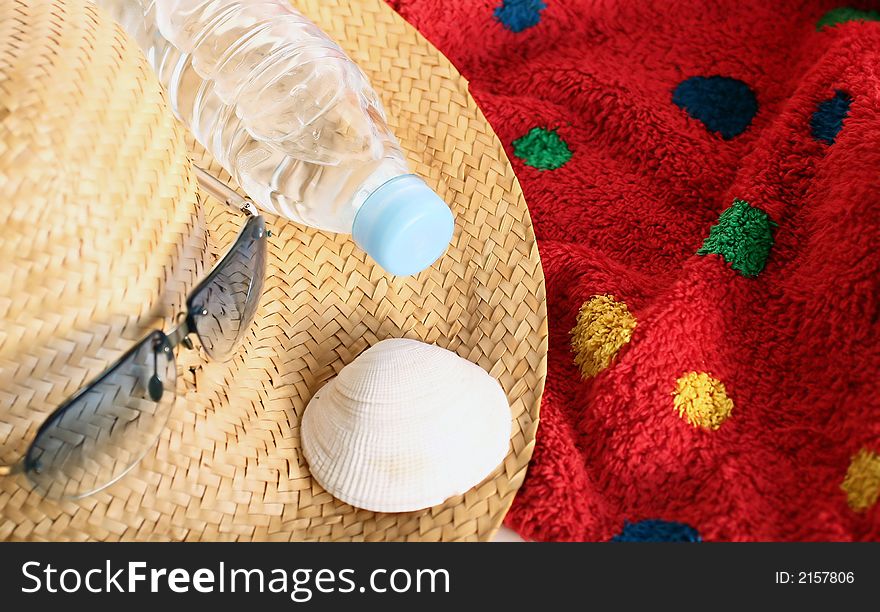 Still-life of things featured to holiday on the beach: straw-hat,sunglasses,towel,sparkling water and shell. Still-life of things featured to holiday on the beach: straw-hat,sunglasses,towel,sparkling water and shell