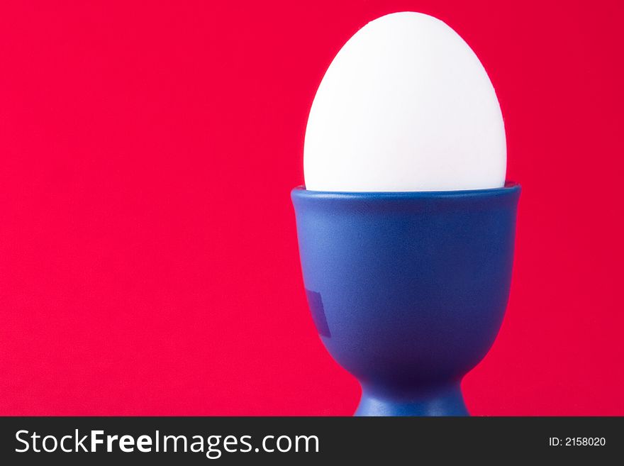 A white egg in a blue egg cup with a red background