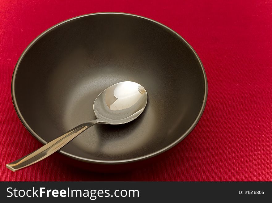Black bowl with spoon on red tablecloth. Black bowl with spoon on red tablecloth
