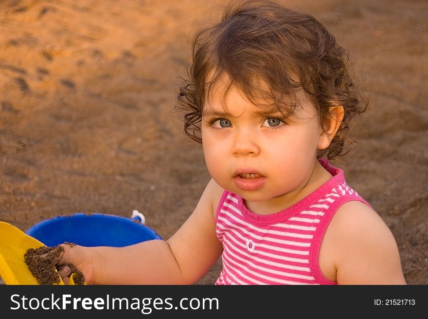 Horizontal upper body shot of a beautiful Caucasian toddler girl playing in sand with a yellow scoop and a blue bucket. Horizontal upper body shot of a beautiful Caucasian toddler girl playing in sand with a yellow scoop and a blue bucket.
