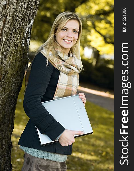 Young woman with notebook smiling at camera in an autumn park