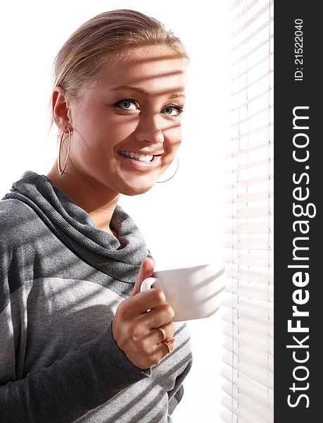 Beautiful woman in gray pullover with cup of coffee beside a window. Beautiful woman in gray pullover with cup of coffee beside a window