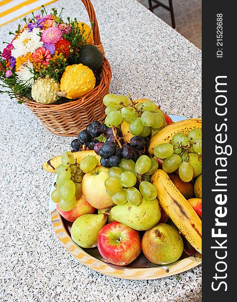 Flower basket and fruit plateau on grey outdoor table.