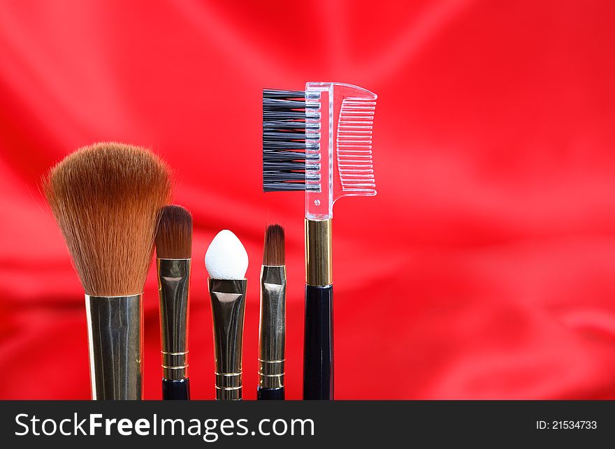 Closeup of makeup brushes set on red silk background