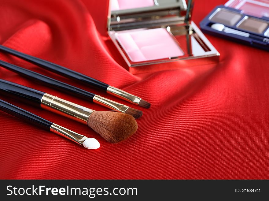 Few makeup brushes and rouge on red silk surface. Few makeup brushes and rouge on red silk surface