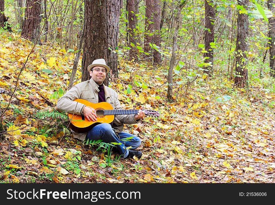 Man is playing a guitar in autumn forest