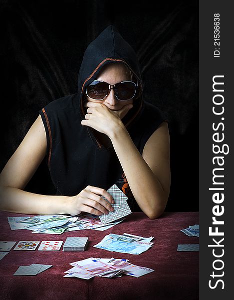 Poker face. Person in sun glasses and hood playing poker at the table with cards and money. Poker face. Person in sun glasses and hood playing poker at the table with cards and money