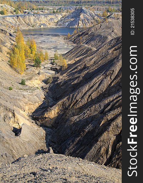 Sand canyon with yellow autumn birches and a lake between hills