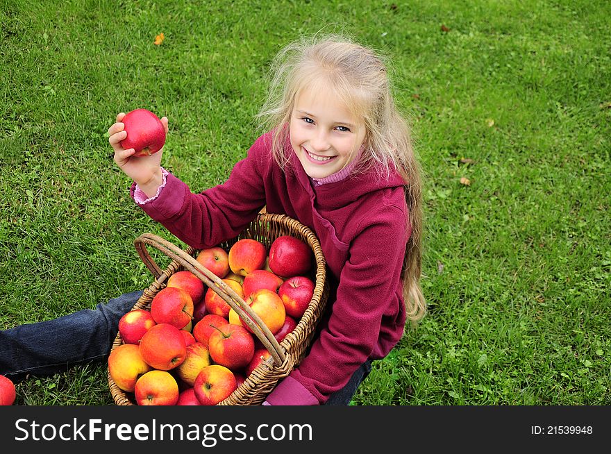 Little girl sitting  on green grass with basket of apples. Little girl sitting  on green grass with basket of apples