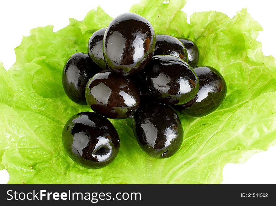 Black ripe olives in oil with a fresh green leaflet of salad
