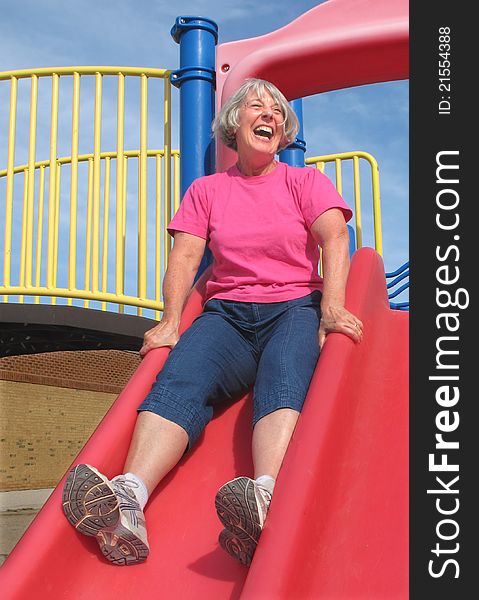 Senior woman with short gray hair, laughing while going down a slide on a childrenâ€™s playground. Senior woman with short gray hair, laughing while going down a slide on a childrenâ€™s playground.
