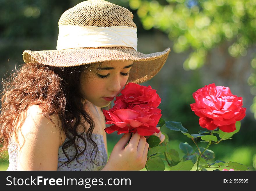 Pretty girl in straw hat smelling red roses in a garden. Pretty girl in straw hat smelling red roses in a garden