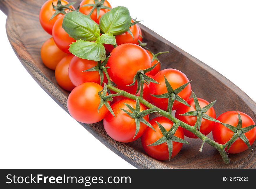 Cherry tomatoes with basil in wood plate isolated on white