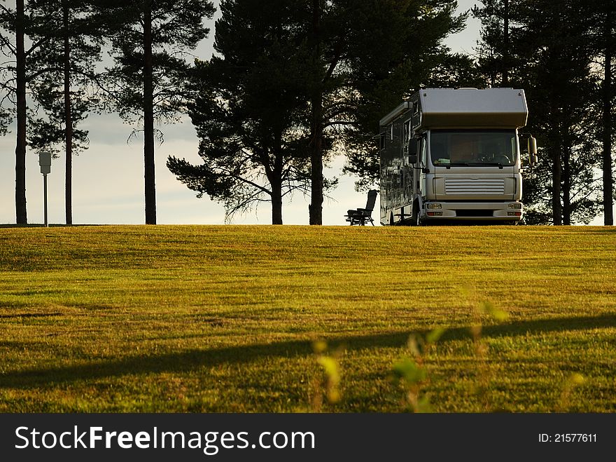 A solitary camping-car is on the field. In the background there are black silhouettes of trees into the sunset. A solitary camping-car is on the field. In the background there are black silhouettes of trees into the sunset.