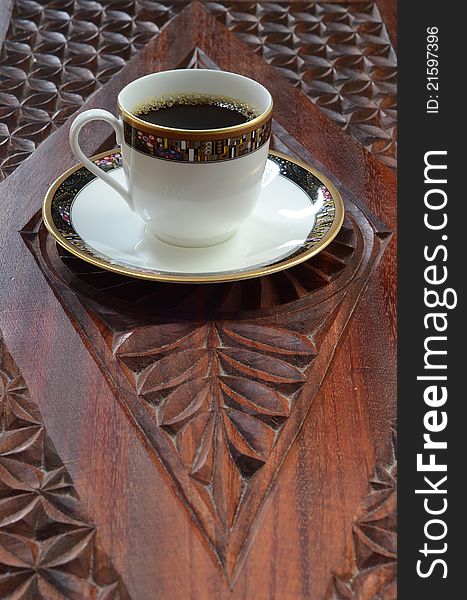 Black coffee in an elegant cup sitting on a carved wood table. Black coffee in an elegant cup sitting on a carved wood table