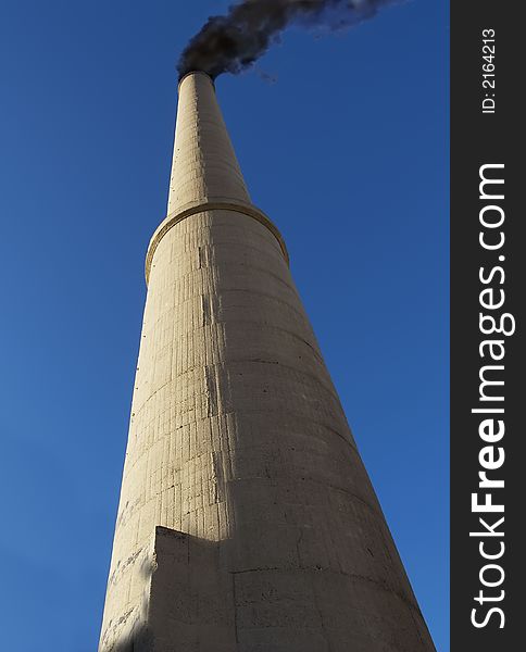 Tall concrete smoke stack and black smoke