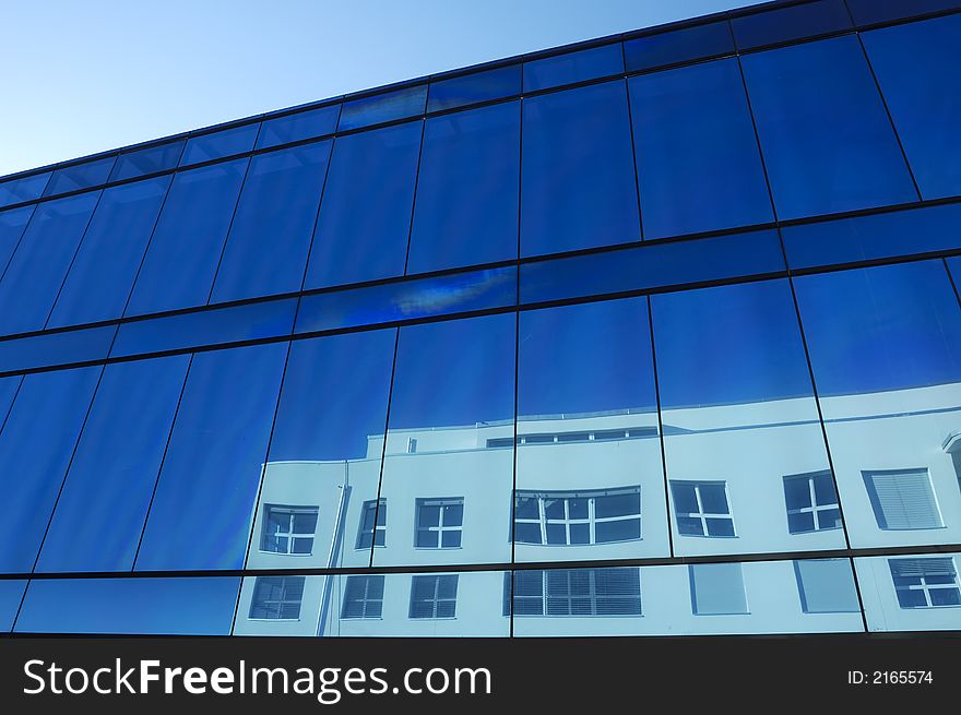 The blue glass facade of an office block with the distorted reflection of a neighbouring building showing in the windows. The blue glass facade of an office block with the distorted reflection of a neighbouring building showing in the windows.