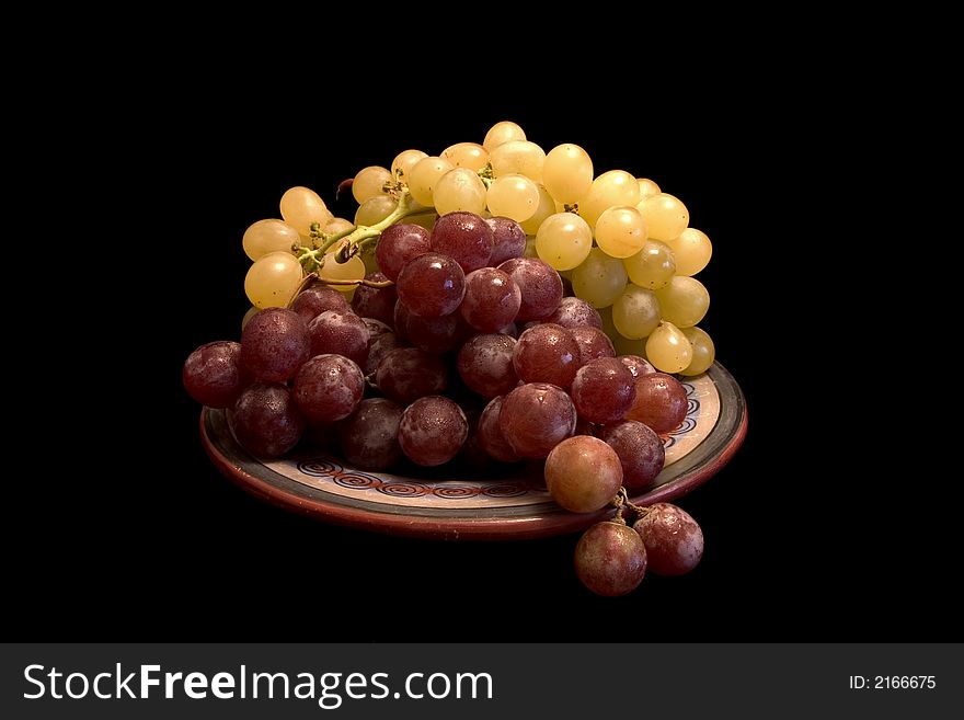 White and black grapes on a plate, isolated on black