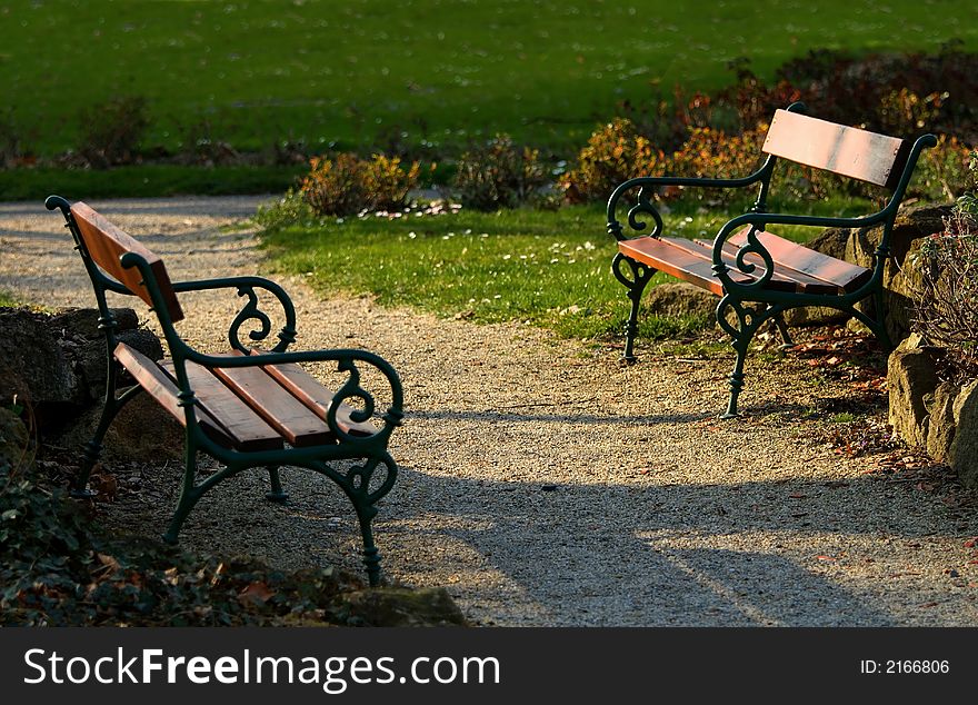 Two facing empty benches in a park at about sunset time. Two facing empty benches in a park at about sunset time.