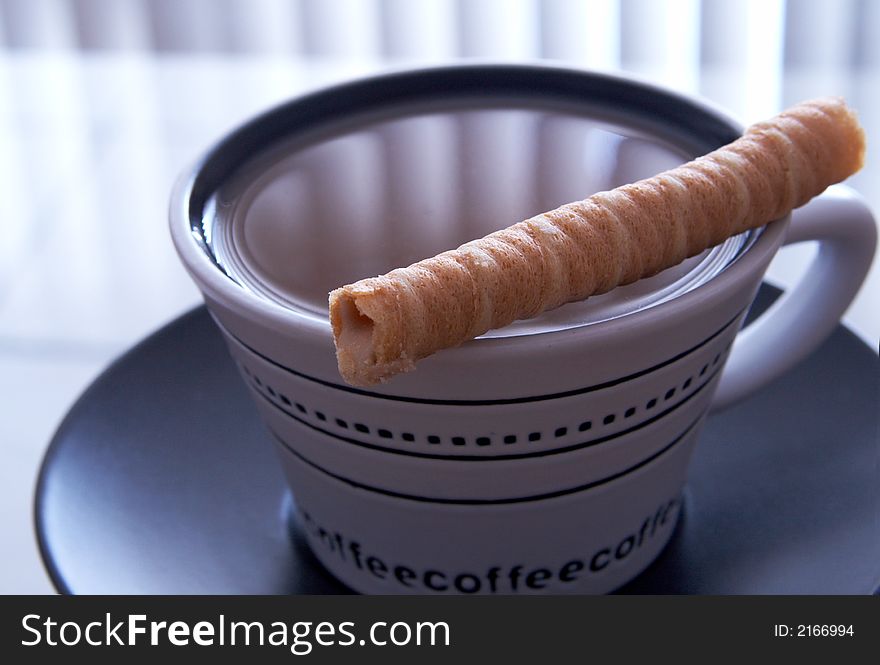 A white cup of coffee on black saucer. A baked swirl is lying on top of the cup. A white cup of coffee on black saucer. A baked swirl is lying on top of the cup.