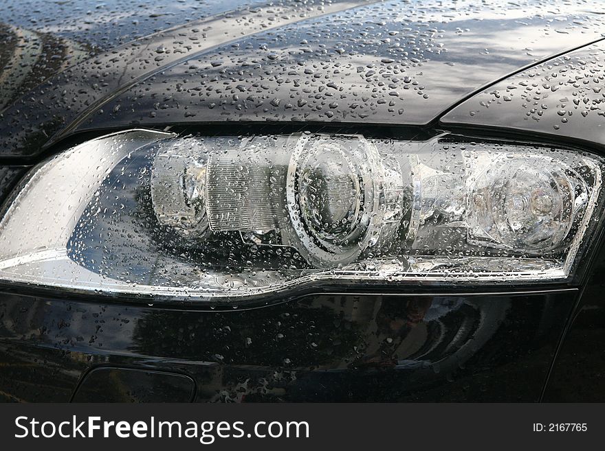 Head lights of a sport black car with drops of rain