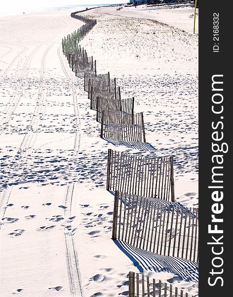 Fences lined up in white sand along the beach forming reflections in the sand to emphasize the geometric shape contrasted to the vehicle tracks next to the curved fence and reflection line. Fences lined up in white sand along the beach forming reflections in the sand to emphasize the geometric shape contrasted to the vehicle tracks next to the curved fence and reflection line