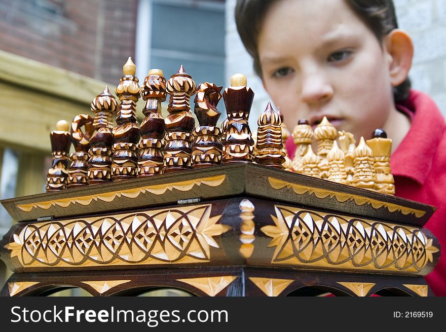 A boy peers over an ornate wooden chess set assembled for the begginning of a match. A boy peers over an ornate wooden chess set assembled for the begginning of a match.
