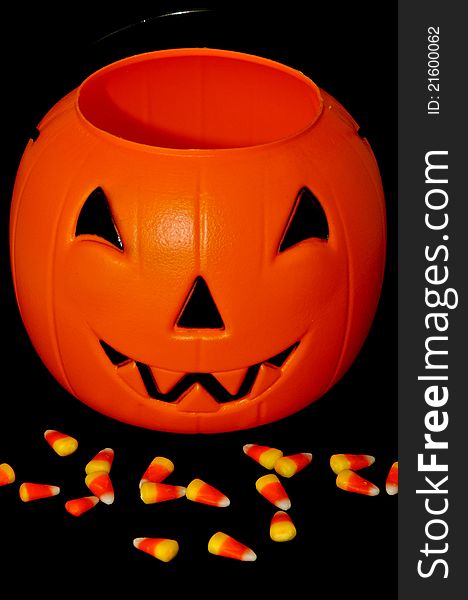 Plastic pumpkin with candy corn in front of it against black background. Plastic pumpkin with candy corn in front of it against black background
