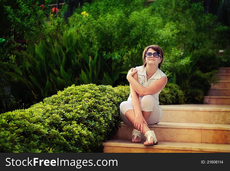 The girl in park in the summer on avenue between bushes of greens wearing spectacles