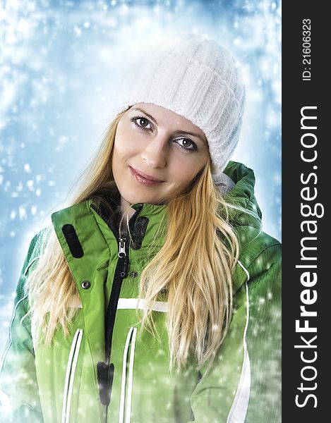 Portrait of young smiling fashion woman in green sport ski jacket and white knitted cap for winter. Snow flakes