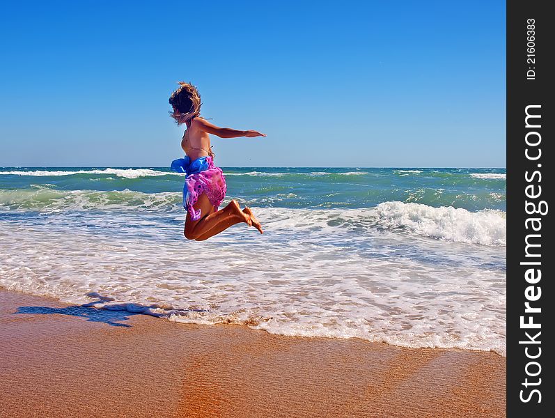 Girl in pareo jumping on the coastline of a stormy sea