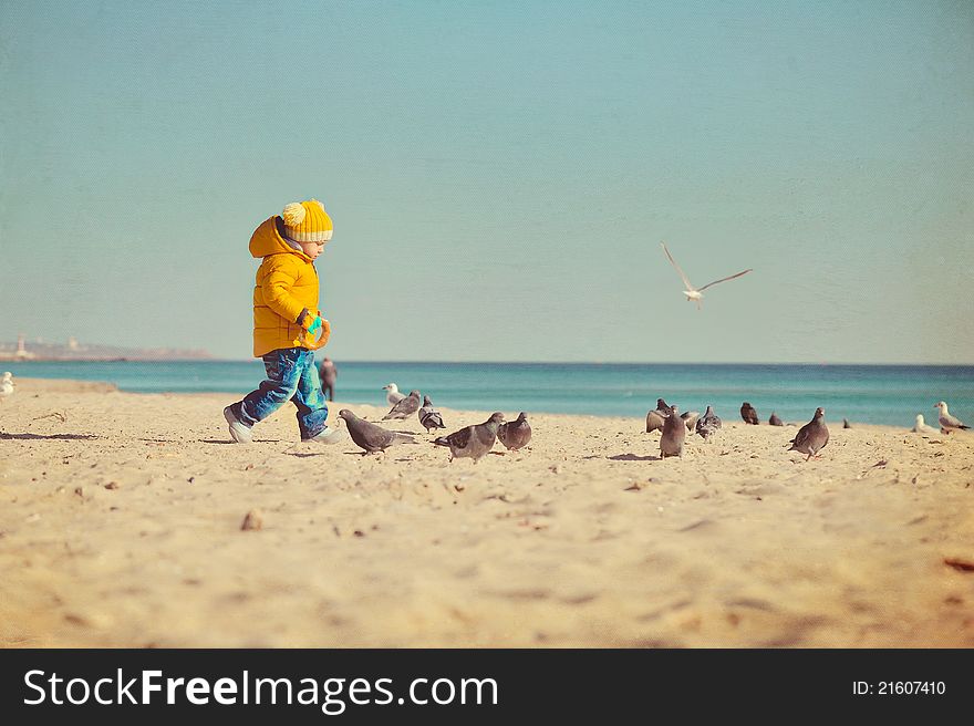 On the seashore the child with pigeons walks. On the seashore the child with pigeons walks