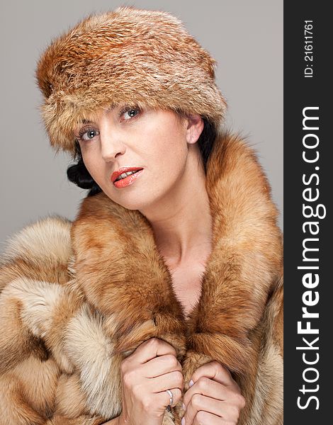 Mature seducing brunette in fox fur  and fox hat on gray background. Mature seducing brunette in fox fur  and fox hat on gray background