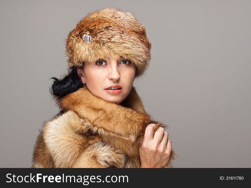 Mature seducing brunette in fox fur  and fox hat on gray background. Intents look. Mature seducing brunette in fox fur  and fox hat on gray background. Intents look