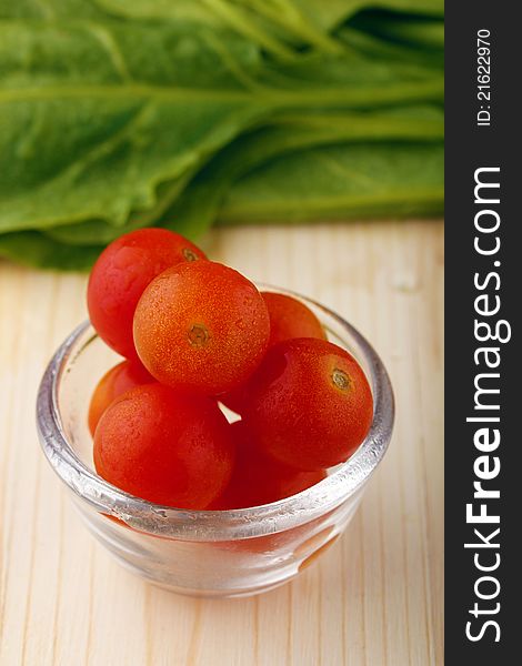 Fresh tomatoes in a bowl and spinach leaves in the background. Fresh tomatoes in a bowl and spinach leaves in the background