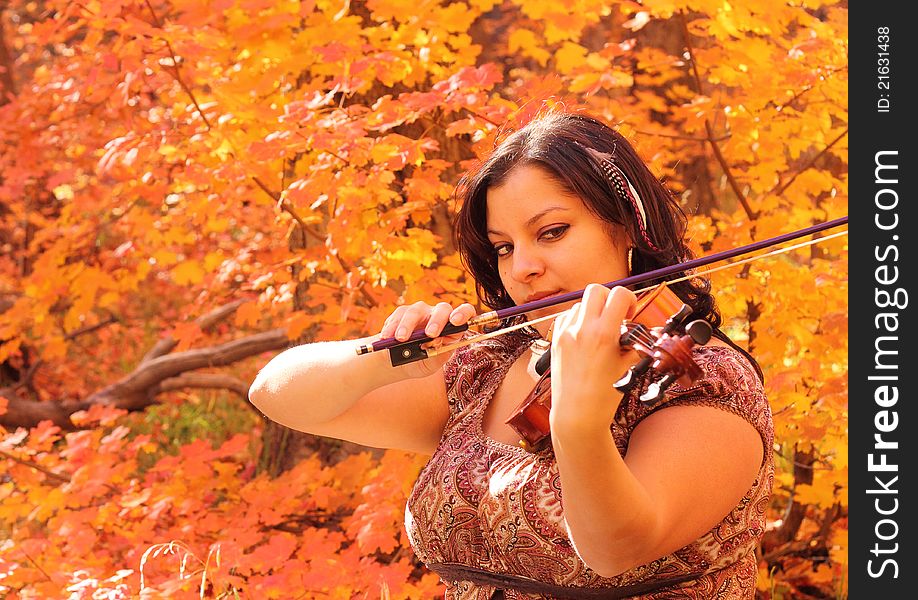 Pretty woman playing her violin with an autumn color backdrop. Pretty woman playing her violin with an autumn color backdrop.