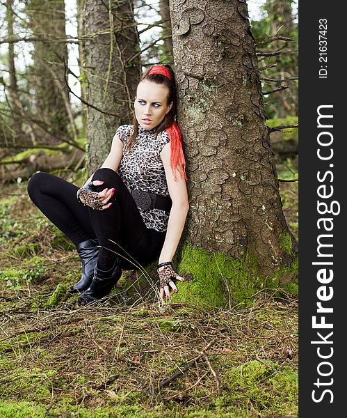 Young woman crouching beside a mossy tree in the forest. Young woman crouching beside a mossy tree in the forest