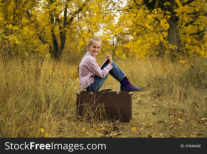 Little girl is reading a book in autumn wood
