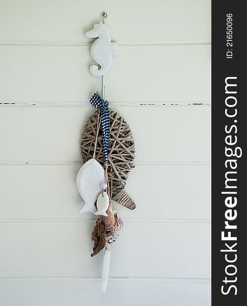 Iron seahorse hook with wooden, soap and reed fish and blue and white check ribbon on a white wall boards. Iron seahorse hook with wooden, soap and reed fish and blue and white check ribbon on a white wall boards.