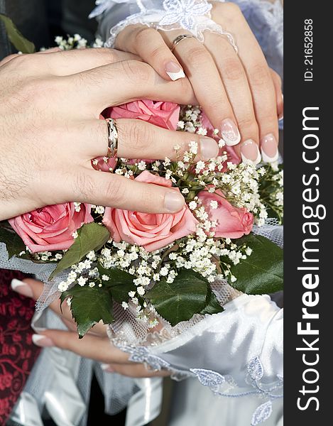 Hand of the bride and hand of the groom with rings over a wedding bouquet against a white dress. Hand of the bride and hand of the groom with rings over a wedding bouquet against a white dress